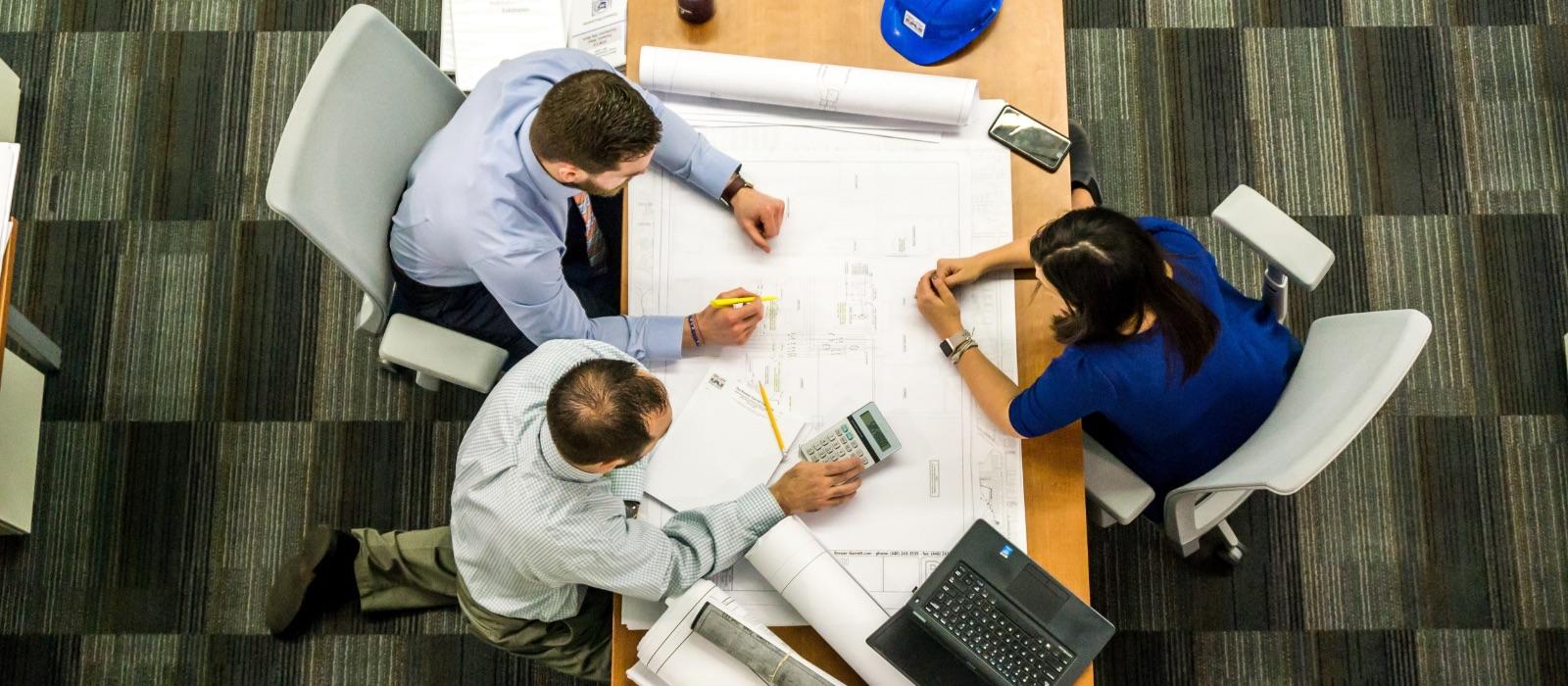 people talking around blueprints on a table